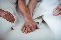 Close-up of senior couple holding hands on bed — Stock Photo