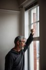 Thoughtful man looking through window at home — Stock Photo