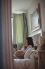 Вагітна жінка дивиться на сонографію на цифровому столі в спальні — стокове фото