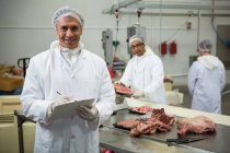 Retrato de açougueiro macho mantendo registros na área de transferência na fábrica de carne — Fotografia de Stock
