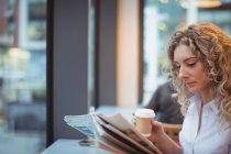 Empresária atenciosa lendo jornal com café no balcão na cafetaria — Fotografia de Stock
