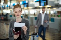 Улыбающаяся деловая женщина проверяет посадочный талон в терминале аэропорта — стоковое фото