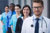 Portrait of smiling doctors standing in row at hospital premises — Stock Photo