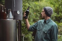 Человек держит бутылку пива, пока делает пиво на пивоваренном заводе — стоковое фото