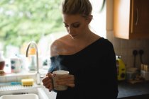 Mulher atenciosa segurando uma xícara de café na cozinha em casa — Fotografia de Stock
