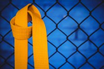 Gros plan de la ceinture jaune karaté accrochée à une clôture en treillis métallique dans un studio de fitness — Photo de stock