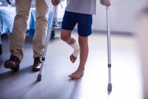 Médico assistindo menino ferido para andar com muletas no hospital — Fotografia de Stock