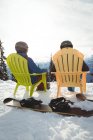 Rückansicht eines Paares, das im Winter auf einem Berg gegen den Himmel sitzt — Stockfoto