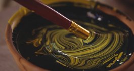 Gros plan du bol de mélange de couleurs avec un pinceau dans un atelier de poterie — Photo de stock