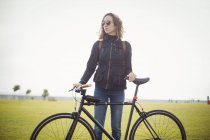 Женщина в солнечных очках держит велосипед в парке — стоковое фото