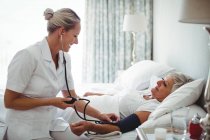 Enfermera revisando la presión arterial de la mujer mayor en casa - foto de stock