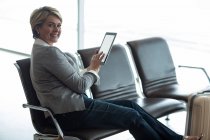 Усміхнена бізнес-леді використовує цифровий планшет в зоні очікування в терміналі аеропорту — стокове фото