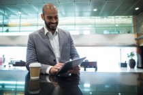 Hombre de negocios sonriente usando tableta digital en la sala de espera en la terminal del aeropuerto - foto de stock