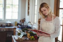 Belle femme lecture livre de recettes dans la cuisine à la maison — Photo de stock