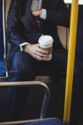 Средняя секция бизнесмена с одноразовой кофейной чашкой проверяет карман блейзера во время поездки на автобусе — стоковое фото