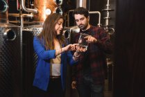 Uomo e donna che esaminano il campione di alcol nella fabbrica di birra — Foto stock