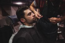 Uomo ottenere barba tagliata da parrucchiere con le forbici in negozio di barbiere — Foto stock