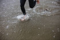 Baixa seção de atleta em terno molhado correndo na praia — Fotografia de Stock