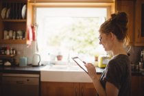 Mulher sorridente usando tablet digital na cozinha em casa — Fotografia de Stock