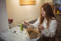 Женщина держит мобильный телефон во время еды в ресторане — стоковое фото