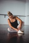 Балерина регулирует чулки, сидя в балетной студии — стоковое фото