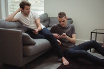Гей пара за допомогою цифрових планшетів і мобільний телефон у вітальні на дому — стокове фото