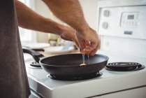 Средняя часть человека разбивает яйцо в сковородке на кухне дома — стоковое фото