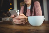 Середній розділ жінки, що використовує мобільний телефон у кафе — стокове фото