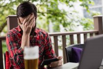 Расстроенный мужчина держит мобильный телефон в баре — стоковое фото