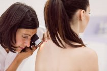 Дерматолог осматривает кожу пациента с дерматоскопом в клинике — стоковое фото
