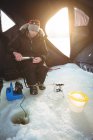Mitte erwachsener Eisfischer gießt Kaffee ins Zelt — Stockfoto