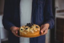 Partie médiane de l'homme tenant gâteau aux myrtilles dans le salon à la maison — Photo de stock