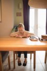 Jolie fille assise à la table et le livre de lecture à la maison — Photo de stock