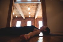 Mujer acostada en la esterilla mientras practica yoga en un gimnasio - foto de stock