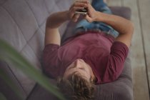 Мужчина лежит на диване и использует мобильный телефон в гостиной — стоковое фото