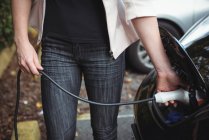 Partie médiane de la femme charge voiture électrique sur la rue — Photo de stock