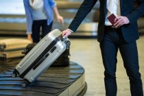 Parte média do empresário que recolhe a sua bagagem na área de recolha de bagagens no terminal do aeroporto — Fotografia de Stock