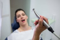 Primo piano del dentista che tiene il pezzo di mano dentale mentre esamina la donna in clinica — Foto stock