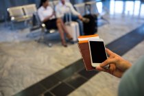 Hand of woman holding smartphone, passport and boarding pass at airport terminal — Stock Photo
