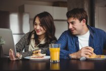 Couple utilisant une tablette numérique tout en prenant le petit déjeuner à la maison — Photo de stock