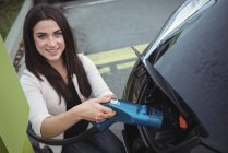 Portrait of beautiful woman charging electric car on street — Stock Photo