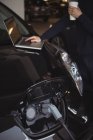Человек с ноутбуком во время зарядки электромобиля в гараже — стоковое фото