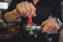 Nahaufnahme einer Kellnerin, die mit einem Stampfer gemahlenen Kaffee in einen Portafilter im Café drückt — Stockfoto
