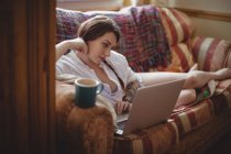 Женщина лежит на диване и пользуется ноутбуком в гостиной дома — стоковое фото