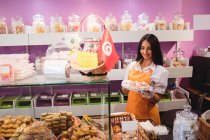 Mujer tendero sosteniendo bandeja de dulces turcos en el mostrador en la tienda - foto de stock