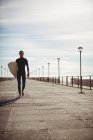 Surfer läuft mit Surfbrett auf Pier am Strand — Stockfoto