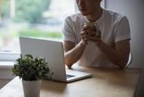 Mann schaut auf Laptop, während er zu Hause Kaffee trinkt — Stockfoto