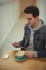 Man using digital tablet while holding coffee cup kept on wooden table in coffee shop — Stock Photo