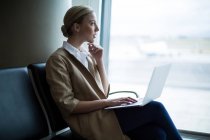 Задумчивая женщина с ноутбуком в зоне ожидания терминала аэропорта — стоковое фото
