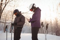Casal de esquiadores usando telefone celular em estância de esqui — Fotografia de Stock